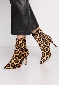 Kožené kotníkové boty s leopardím potiskem v béžové a černé barvě, s špičatou špičkou a jehlovým podpatkem, vyrobené z texturované tkaniny se zipovým uzávěrem.
