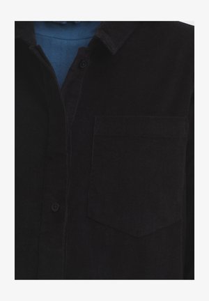 Zwarte corduroy overhemd met een zak, knoopsluiting en een puntkraag. Getextureerde stof met zichtbare ribbels, gedeeltelijk bedekt door een blauwe laag eronder.