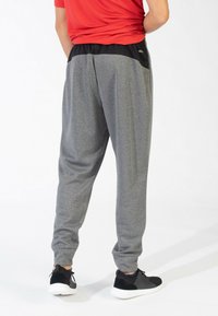 Grijze joggers met een gestructureerde afwerking, elastische tailleband en zijzakken, gecombineerd met zwarte sportschoenen. Achtergrond is effen wit.