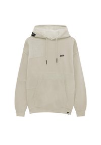 Sweat à capuche beige avec un design texturé, comprenant une poche avant, des cordons de serrage et un petit logo sur la poitrine. Tissu doux, coupe décontractée.