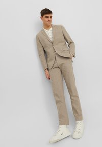 Completo beige chiaro con giacca a un bottone e pantaloni slim-fit. Abbinato a una camicia bianca con colletto e sneakers bianche. Tessuto dalla consistenza morbida.