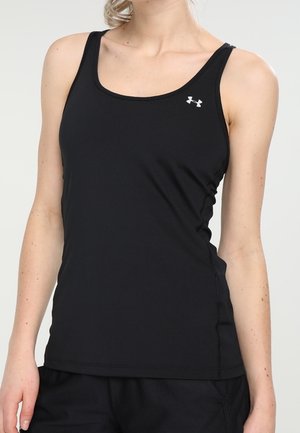 Kvinde iført en tætsiddende sort ærmeløs sportstop med et lille hvidt Under Armour-logo på brystet, kombineret med sorte bukser.