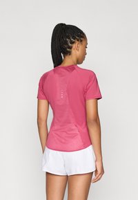 Haut de sport à manches courtes en rose, avec un panneau arrière texturé, un ourlet incurvé et des détails réfléchissants, associé à un short blanc.