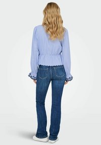 Blauwe gestreepte blouse met gerimpelde manchetten en een getailleerde taille, gecombineerd met donkerblauwe jeans. Witte sneakers maken de outfit af.