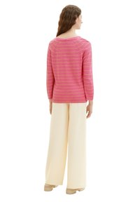 Rosa gestreifter Pullover aus leichtem Stoff, runder Ausschnitt und Dreiviertelärmel. Kombiniert mit weitgeschnittenen, cremefarbenen Hosen und beigen Schuhen.