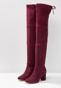 Botas de ante sintético burdeos altas con punta afilada, tacón grueso y lazo ajustable en la parte superior para un buen ajuste. Textura suave.