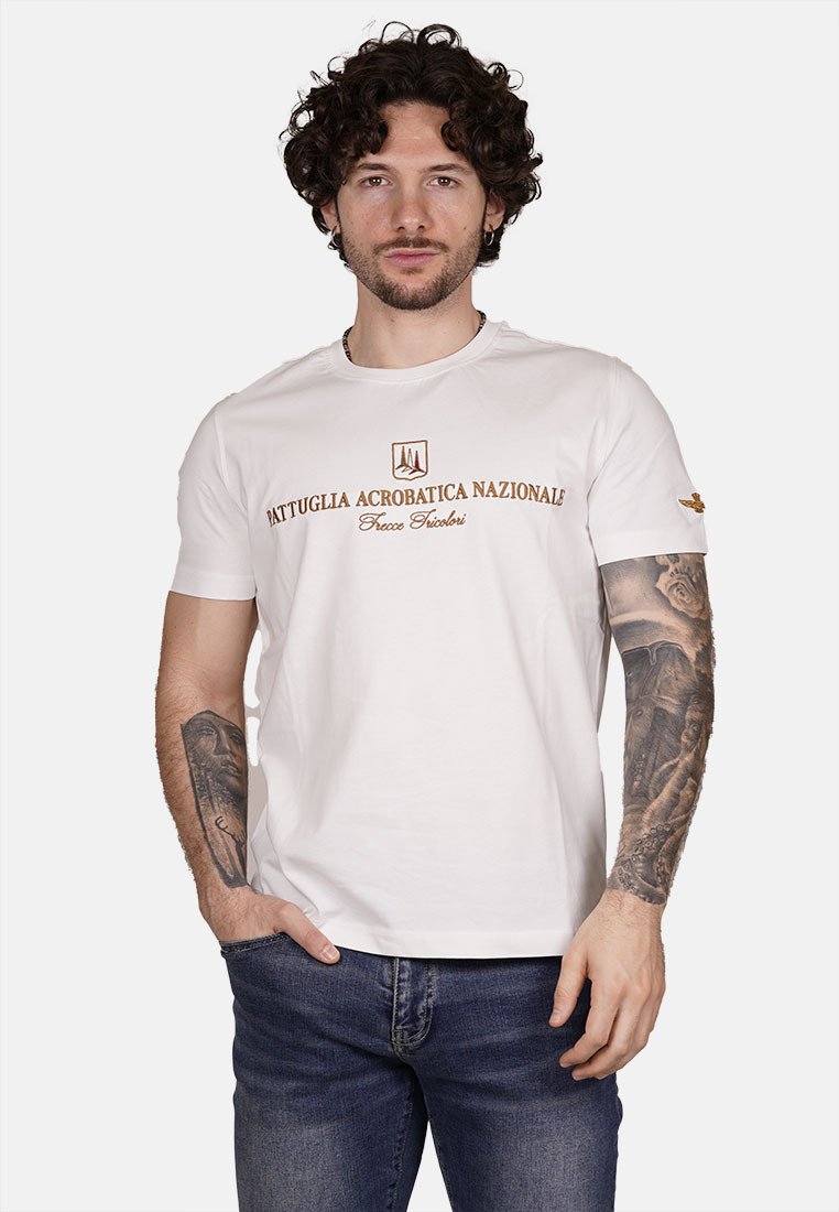 T-shirt bianca in cotone con la scritta "PATTUGLIA ACROBATICA NAZIONALE" in lettere marroni, scollo rotondo e maniche corte. Vestibilità casual senza fantasie.