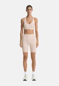 Beige sports bra with a deep V-neckline and crossover design, paired with high-waisted beige bike shorts, made of smooth, stretchy fabric.