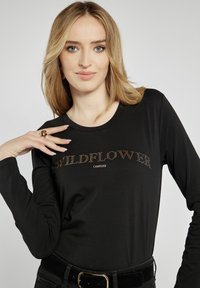 Czarna bluzka z długim rękawem z centralnym wzorem z napisem "WILDFLOWER" w kryształkach i "CAMPIONE" poniżej. Gładka faktura, okrągły dekolt.