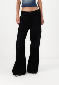 Svarte vide jeans med høy midje, laget av denim. Har frontlommer og en slitt tekstur med subtil falming.