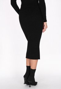 Zwarte geribbelde midi-rok met metallic vlekken. Taillevorm, rechte zoom, gecombineerd met zwarte enkellaarsjes. Gladde textuur, elegante uitstraling.