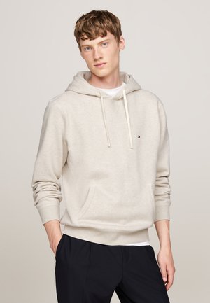 Helle beige Kapuzenjacke aus weichem Stoff, mit einer vorderen Tasche, Kordeln, gerippten Bündchen und einem kleinen Logo auf der Brust.