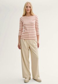 Striped long-sleeve top in light pink and red, paired with beige wide-leg trousers and beige footwear. Simple design with round neckline.