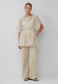 Lichte doorschijnende crèmekleurige blouse met een geraffineerde taille. Gecombineerd met textuurbeige wijde broek met een geometrisch patroon. Zwarte sandalen.