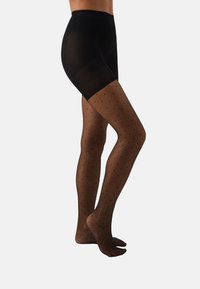 Μαύροι αδιαφανείς σορτς σε συνδυασμό με διάφανες μαύρες καλσόν με μοτίβο πουά, αναδεικνύοντας μια λεία υφή και εφαρμοστό σχέδιο.