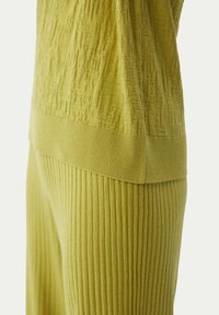 Limegrön stickad set med en texturerad pullover med geometriskt mönster och ribbade högmidjade byxor, båda med en mjuk finish.