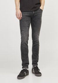 Jean noir ajusté avec une finition usée, des surpiqûres contrastées et un design à cinq poches, associé à des baskets noires avec des accents blancs.