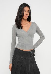 Haut gris à manches longues avec effet cache-cœur en texture côtelée et décolleté plongeant en V. Associé à une jupe en denim noire plissée taille haute avec des accessoires argentés.