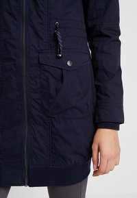 Granatowa parka z zamkiem z przodu, elastycznymi mankietami i ściągaczem w talii. Posiada kieszonkę na piersi oraz teksturowany materiał.