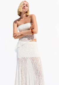 White lace two-piece outfit featuring a strapless top and a long skirt. The fabric has a textured pattern and a flowing silhouette.