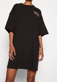 Czarna, oversize sukienka t-shirt z bawełny, z okrągłym dekoltem i czerwonym logo na lewej piersi. Krótkie rękawy i gładki design.