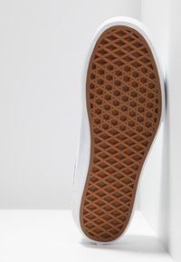 Baskets blanches présentant une semelle en caoutchouc texturée avec un motif en losanges. La tige présente une surface lisse et une silhouette fine.