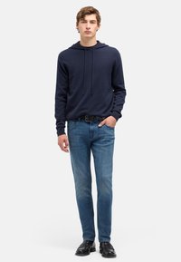 Granatowa bluza z kapturem i sznurkami, noszona na czarnej koszuli; w połączeniu z jasnoniebieskimi dżinsami i czarnymi eleganckimi butami, stojąc na białym tle.