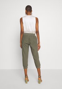 Haut sans manches gris clair avec dos plissé, associé à un pantalon style jogger vert olive doté de poignets côtelés et d'une taille élastique.