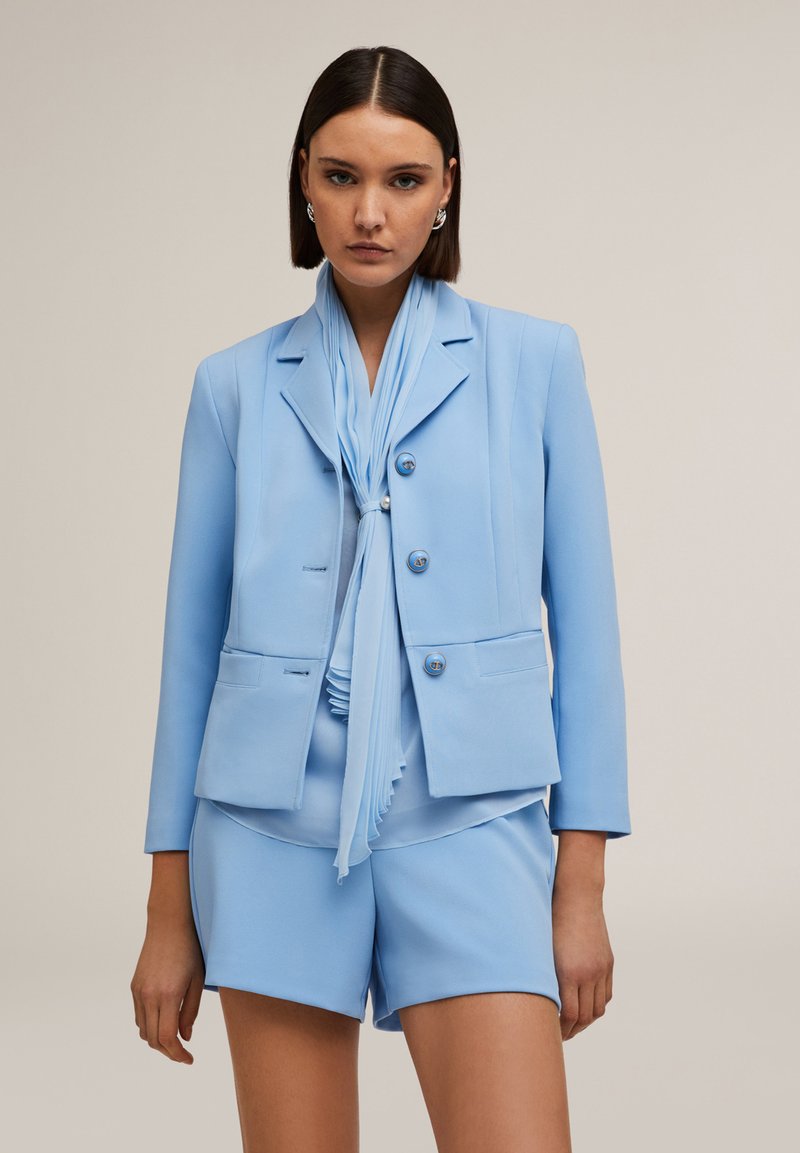 Ljusblå blazer med matchande shorts, med en skräddarsydd design, knappar och en veckad scarf. Slät tyg med minimalistiska detaljer.