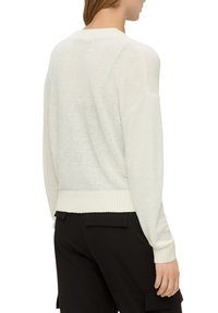 Vit stickad tröja med lös passform, ribbat nederkant och muddar samt en subtil textur. Bärs över svarta byxor och visar dess bakvy.