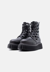 Bottes à plateforme noires avec semelles épaisses côtelées et design découpé en treillis sur le dessus, présentées sur un fond blanc.