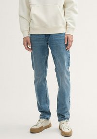 Jeans de mezclilla azul claro con un corte recto, un desgaste sutil y un diseño clásico de cinco bolsillos, combinados con zapatillas bajas beige.