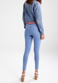 Lichtblauwe skinny jeans van denim met een rafelige zoom, gecombineerd met een cropped lichtblauwe denim jas. De outfit bevat een roze top eronder.