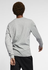 T-shirt de algodão cinza de mangas longas, com gola redonda, corte relaxado e detalhes de costura mínimos, combinado com calças pretas.