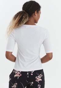 Hvid ribbet kortærmet top med rund halsudskæring, med en glat overflade. Bært med bukser i sort med blomsterprint.