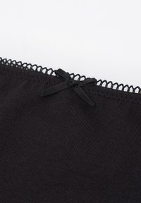 Černá bavlněná tkanina s ribbovanou strukturou, se zdobným krajkovým lemem nahoře a malou mašlí uprostřed.