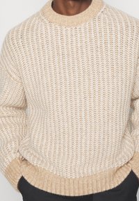 Strickpullover in Creme und Beige, mit strukturiertem Design, Rundhalsausschnitt und gerippten Säumen. Lockerer Schnitt mit überschnittenen Schultern.