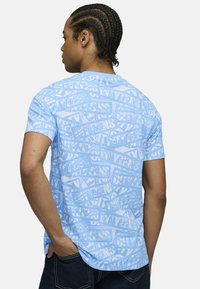 Ljusblå kortärmad t-shirt med ett upprepat grafiskt mönster av vit text och former, tillverkad av mjukt tyg.