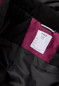 Musta ja violetti takin sisäosa, jossa on hoito-ohjeet. Etiketissä on koko tietoja ja kenttiä nimille. Pehmeä fleece-kangas näkyvissä.