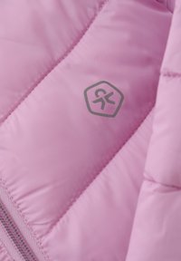 Lys pink pufferjakke stof med quiltet tekstur, prydet med et hexagonalt logo i grå og en synlig lynlås. Glat finish og syninger.
