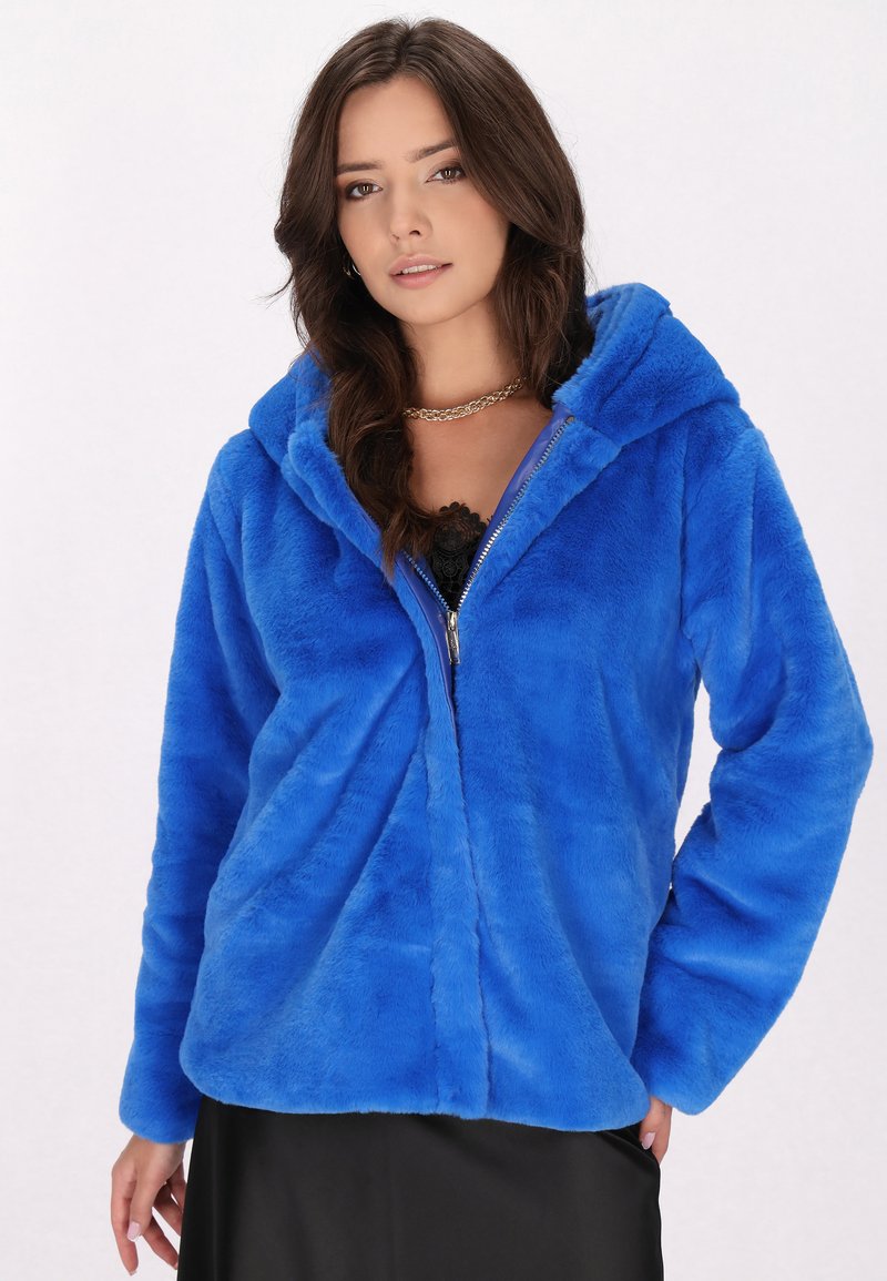 Hoodie in finta pelliccia blu con zip frontale, maniche lunghe e cappuccio largo. Tessuto morbido e vestibilità comoda. Abbbinato a un top nero.