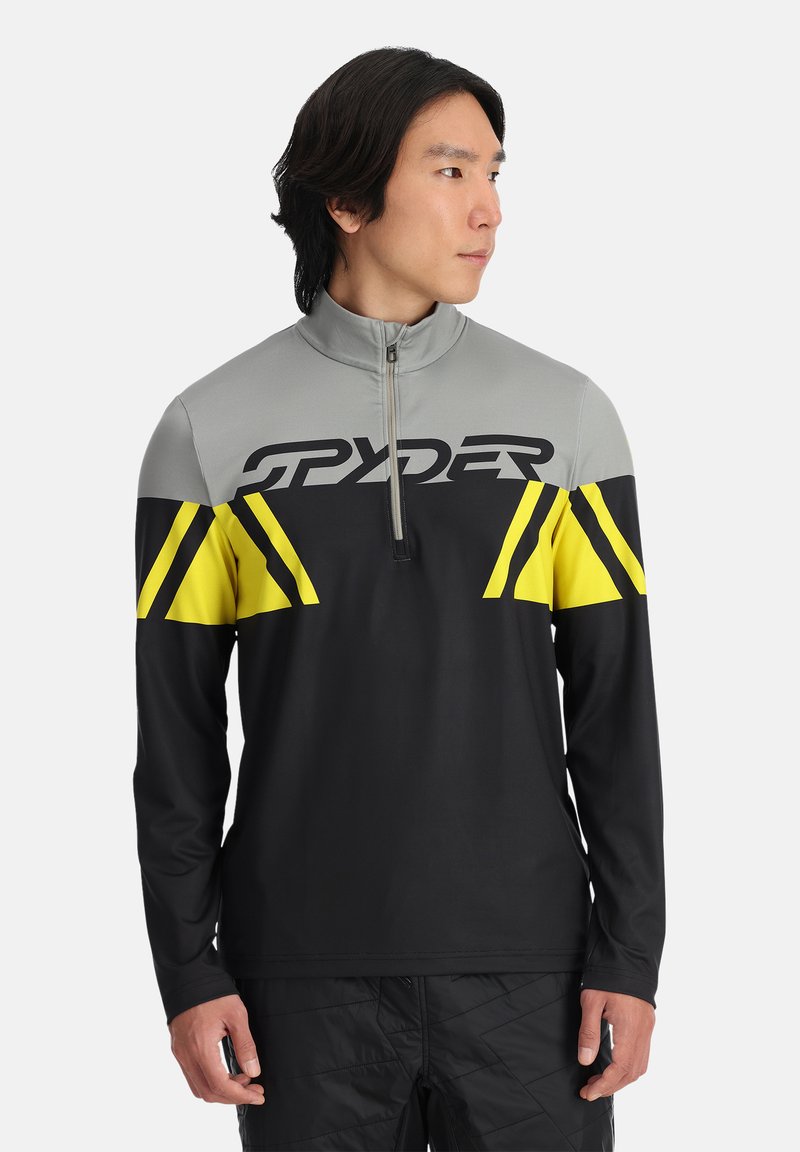 Zwart langemouwen top met grijze kraag en gele accenten. Heeft een kwart rits en het "SPYDER"-logo over de borst in dikke letters.