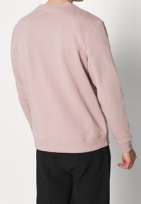 Sudadera de cuello redondo rosa con cuello y puños acanalados. Diseño sencillo con una textura suave y sin logotipos ni patrones visibles.