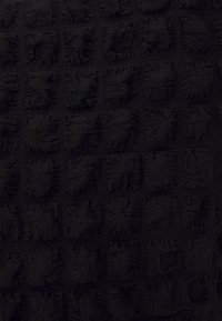 Teksturowana czarna tkanina z warkoczowym wzorem, zawierająca uniesione kwadraty i gładkie sekcje, wykonana z miękkiego materiału dzianinowego.