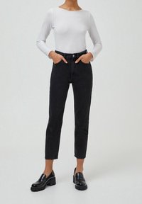 Jean noir taille haute avec une coupe slim et des jambes droites, en denim, associé à un haut blanc ajusté à manches longues et des mocassins noirs.