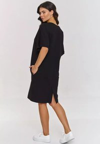 Czarna sukienka z krótkim rękawem o luźnym kroju, z bocznymi kieszeniami i rozcięciem z tyłu, zapewniającym swobodę ruchów. Połączona z białymi sneakersami.