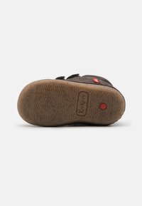 Suela de zapato de ante negro con agarre de goma texturizada. Presenta un logo de Kickers y un punto de acento rojo. Ligeramente usado con suciedad visible.