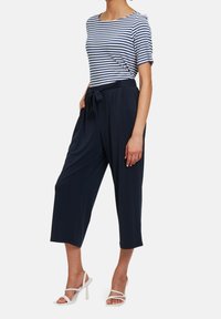 Mörkblå vida cropped-byxor med knytmidja, matchat med en mörkblå och vit randig kortärmad topp. Modell som bär vita högklackade sandaler.