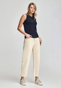 Granatowy top bez rękawów z okrągłym dekoltem, zestawiony z kremowymi spodniami typu wide-leg i beżowymi sneakersami, podkreślający swobodny i zrelaksowany styl.