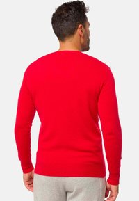 Pull en tricot rouge à manches longues, avec des poignets et un ourlet côtelés. Texture lisse, design classique à col rond et coupe ajustée visible de dos.
